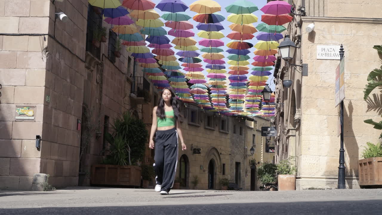 여름 햇살 아래 형형색색의 우산으로 뒤덮인 거리를 행복하게 달리는 귀여운 십대 소녀