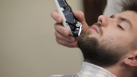 Client-with-black-beard-during-beard-shaving-in-barber-shop.-Groom,-masculine