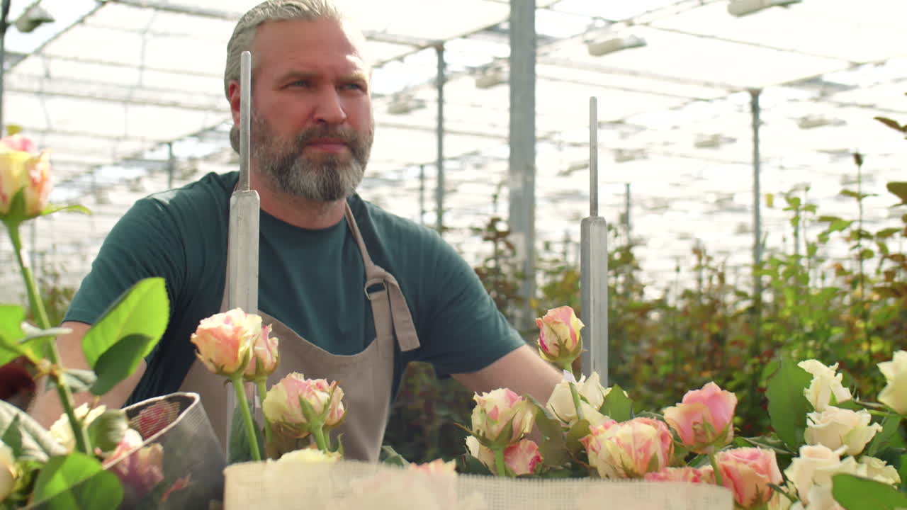 Middelaldrende mann skyver tralle med blomster gjennom drivhus