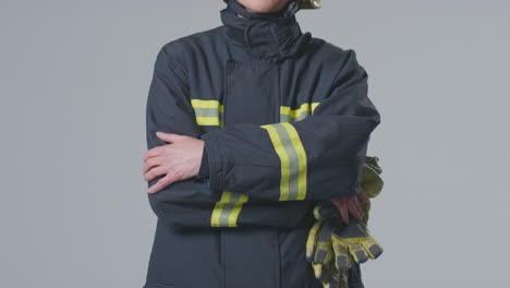 full length studio portrait of smiling mature female firefighter wearing helmet on plain background