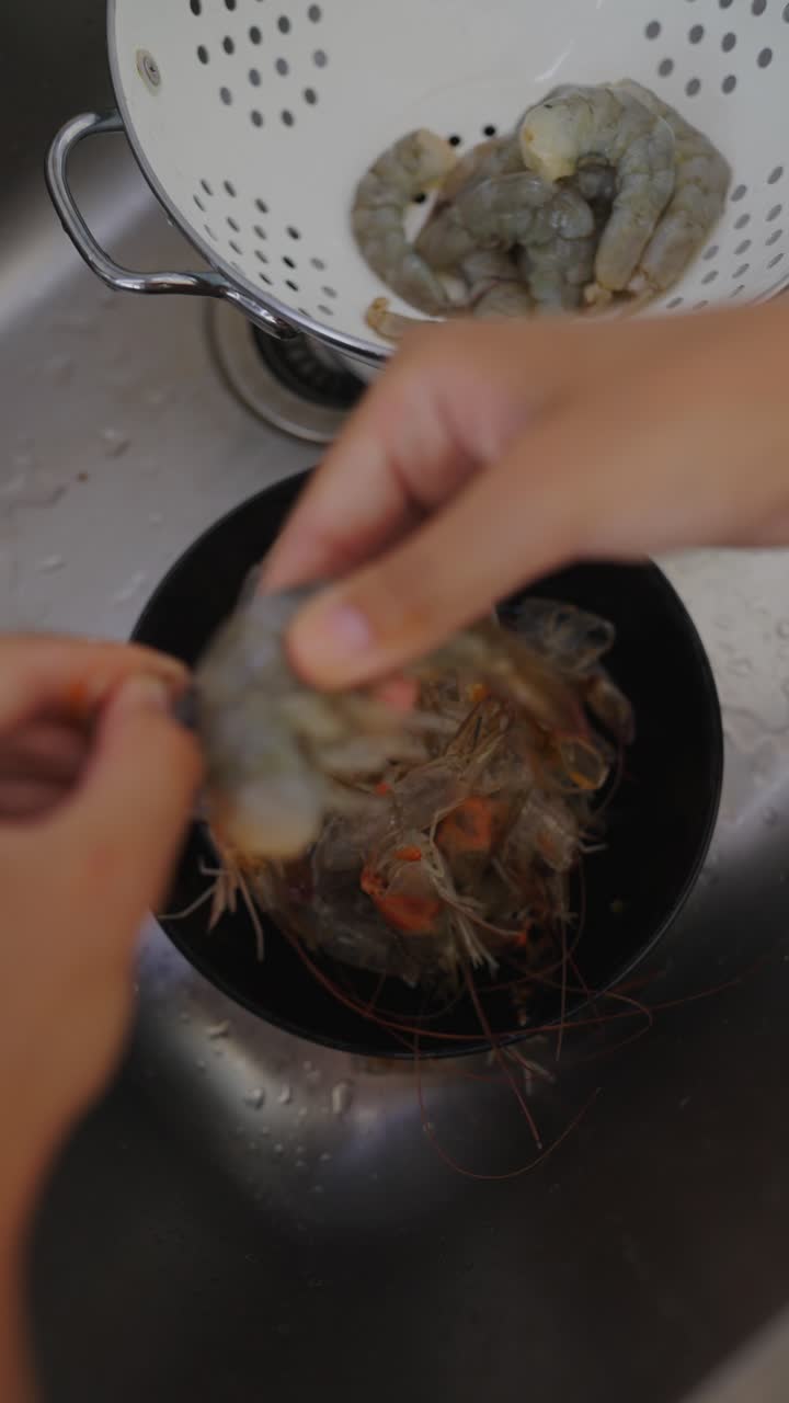 Hands peeling raw shrimp in a kitchen sink