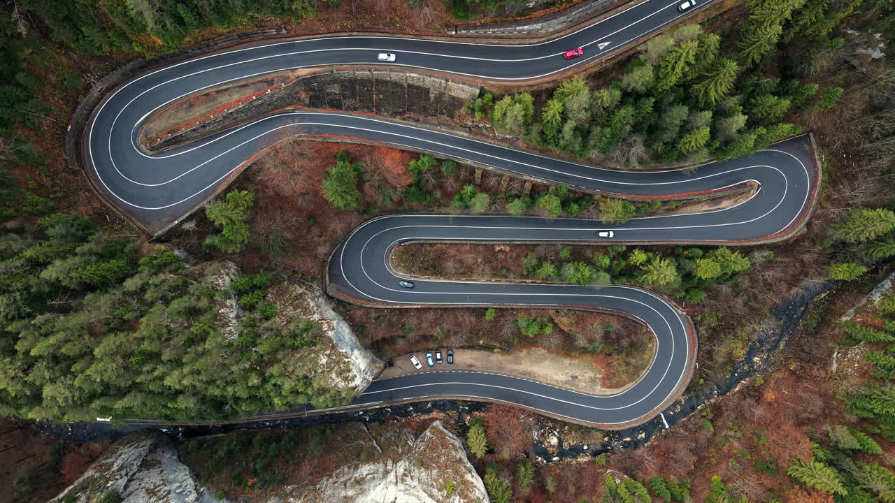 Aerial drone view of nature in Romania. Carpathian mountains, serpentine road with cars in the valley, rocky hills covered with lush forest