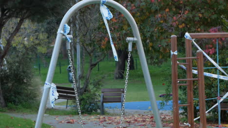 barrier tape tied on the swing at empty playground - covid-19 lockdown - static shot