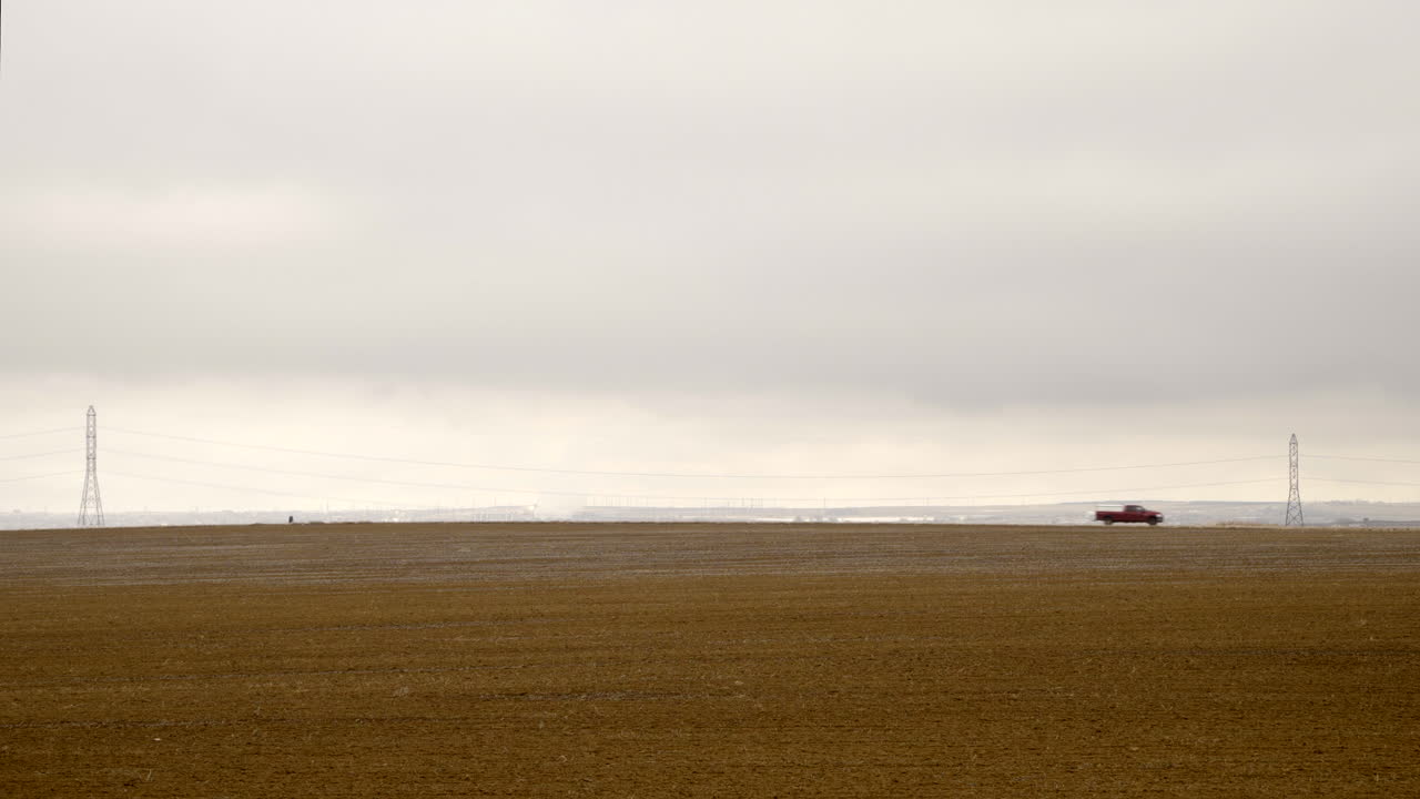 Pickup-truck kører fra venstre mod højre på en landvej i et tørt landbrugslandskab om vinteren, statisk totalbillede.