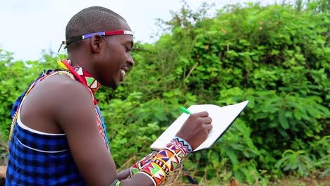 african male, smiling while writing notes in a hes diary, wearing tribal gear
