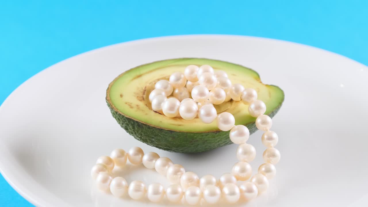 파란색 배경에 색 접시에 진주와 함께 아보카도 반. 패션 음식 디자인