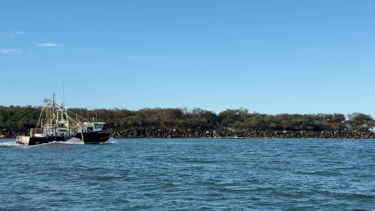 Fishing trawler moves steadily along river channel under clear blue sky, wide static shot