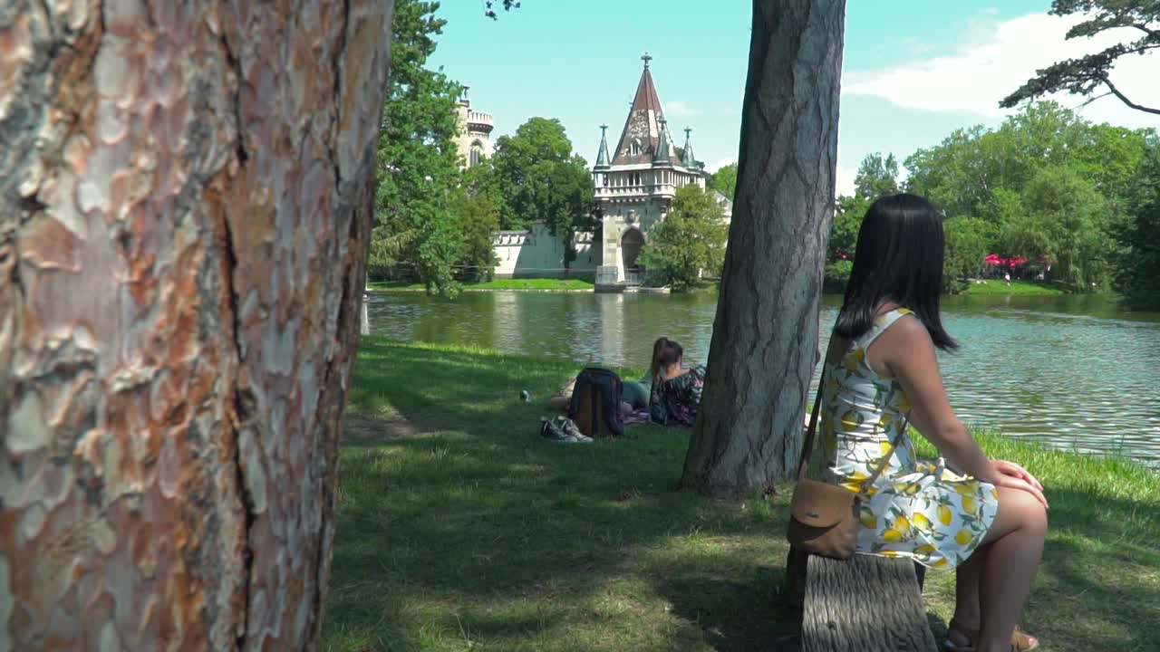 revelación de diapositivas de una chica vestida de verano sentada en un banco del parque con el telón de fondo del castillo de laxenburg cerca de viena