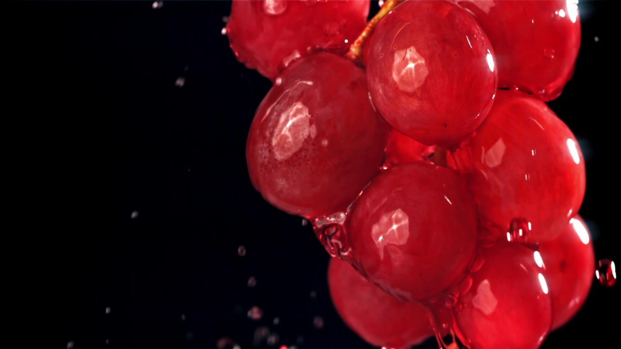 Uva rossa fresca con schizzi d'acqua su sfondo nero.