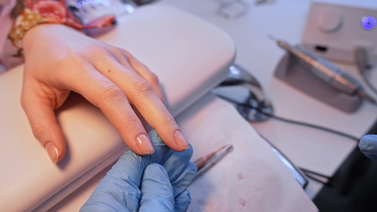Plan large d'un salon de manucure où une prothésiste ongulaire applique une finition brillante, capturant le déroulement calme de la manucure, le soutien de la main de la cliente et des soins de beauté professionnels soignés.