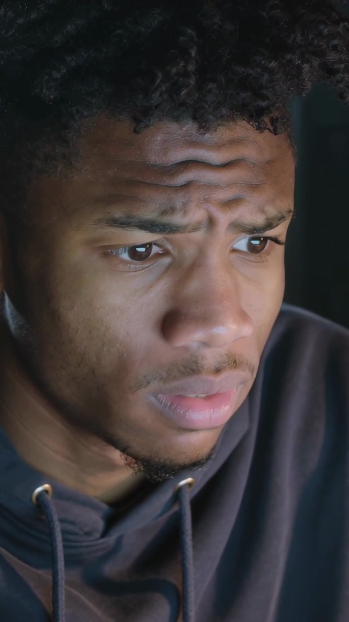 Vertical video: Alert arriving, man in hoodie leaning toward laptop at desk, rubbing forehead
