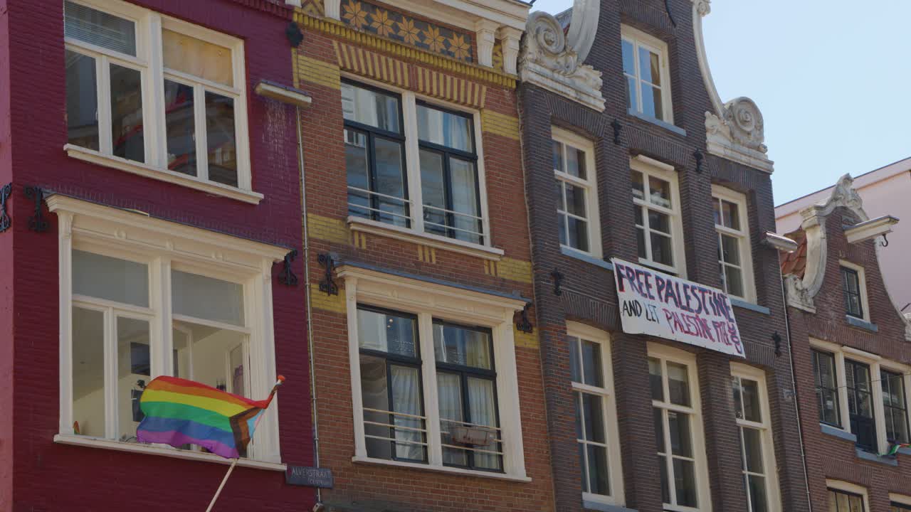 Rainbow flag waves from window, protest banner reads 'Free Palestine', sunny day, static camera