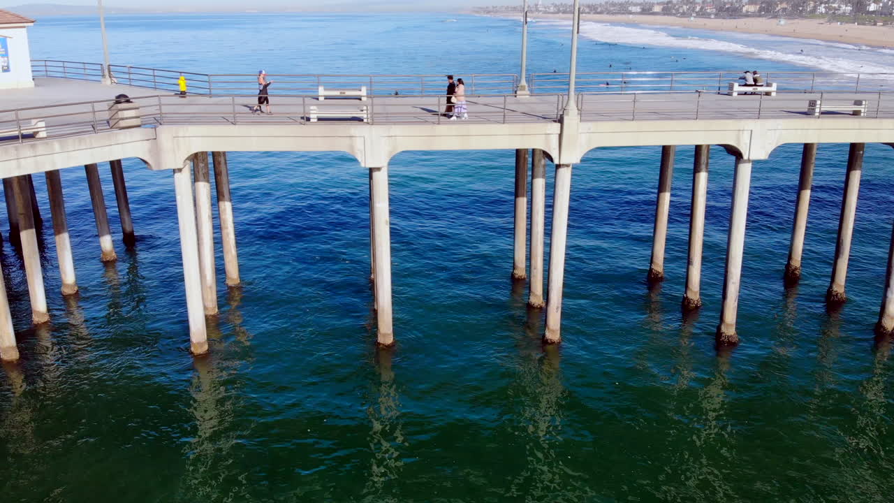 서퍼와 함께 공중 4k 드론으로 헌팅턴 비치 부두 말뚝과 태평양의 물로 날아가세요 - 파도를 배경으로