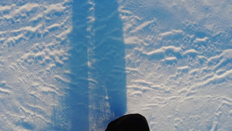 slowmotion of a person walking and kicking snow with long shadows from the legs