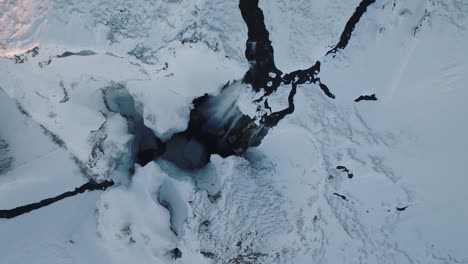 Aerial-top-view-of-a-winter-landscape-covered-in-snow,-over-Skogafoss-waterfall,-in-Iceland,-at-dusk