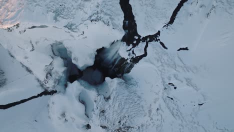 vista aérea superior de un paisaje invernal cubierto de nieve, sobre la cascada de skogafoss, en islandia, al atardecer