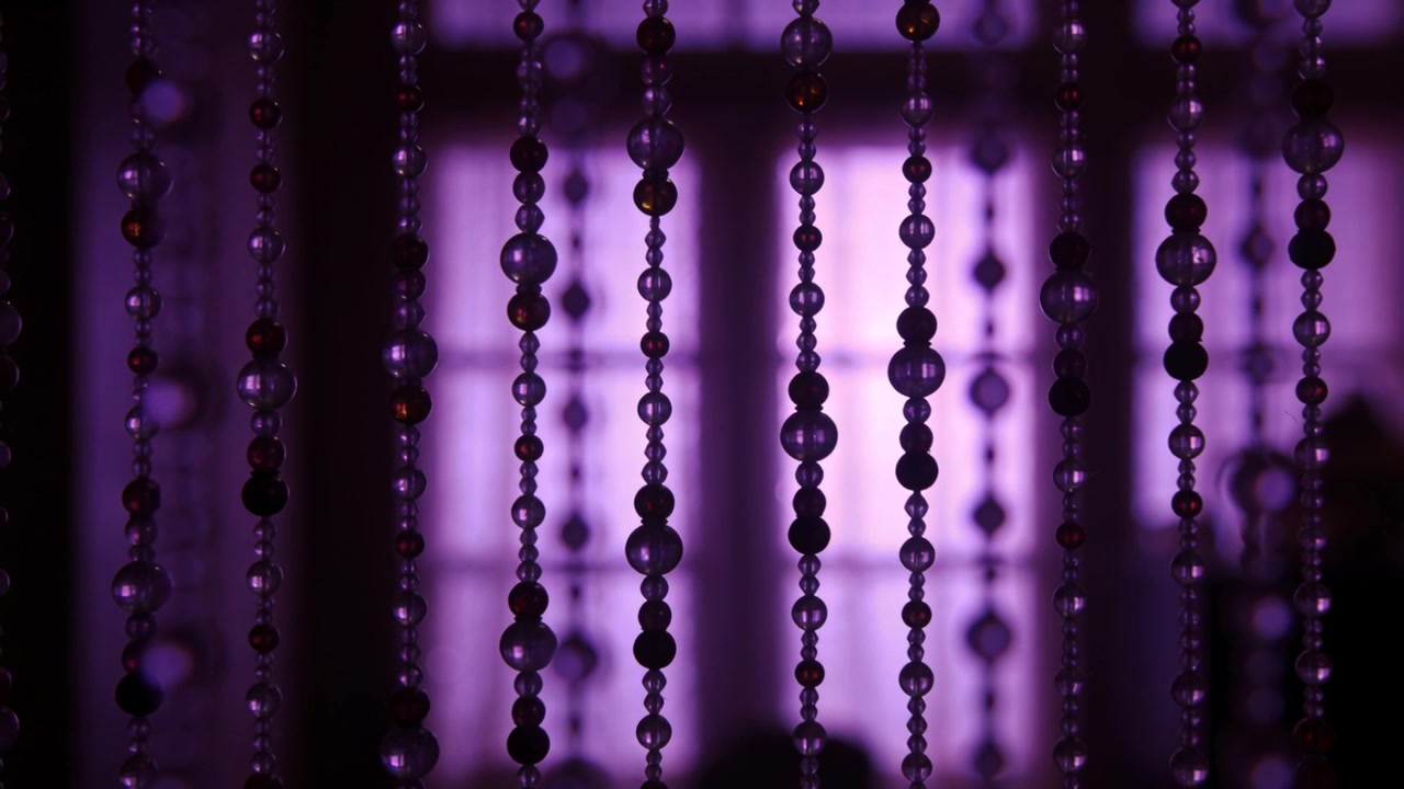 Swaying beaded strands shifting in front of window panes, subtle focus shifts moving highlights