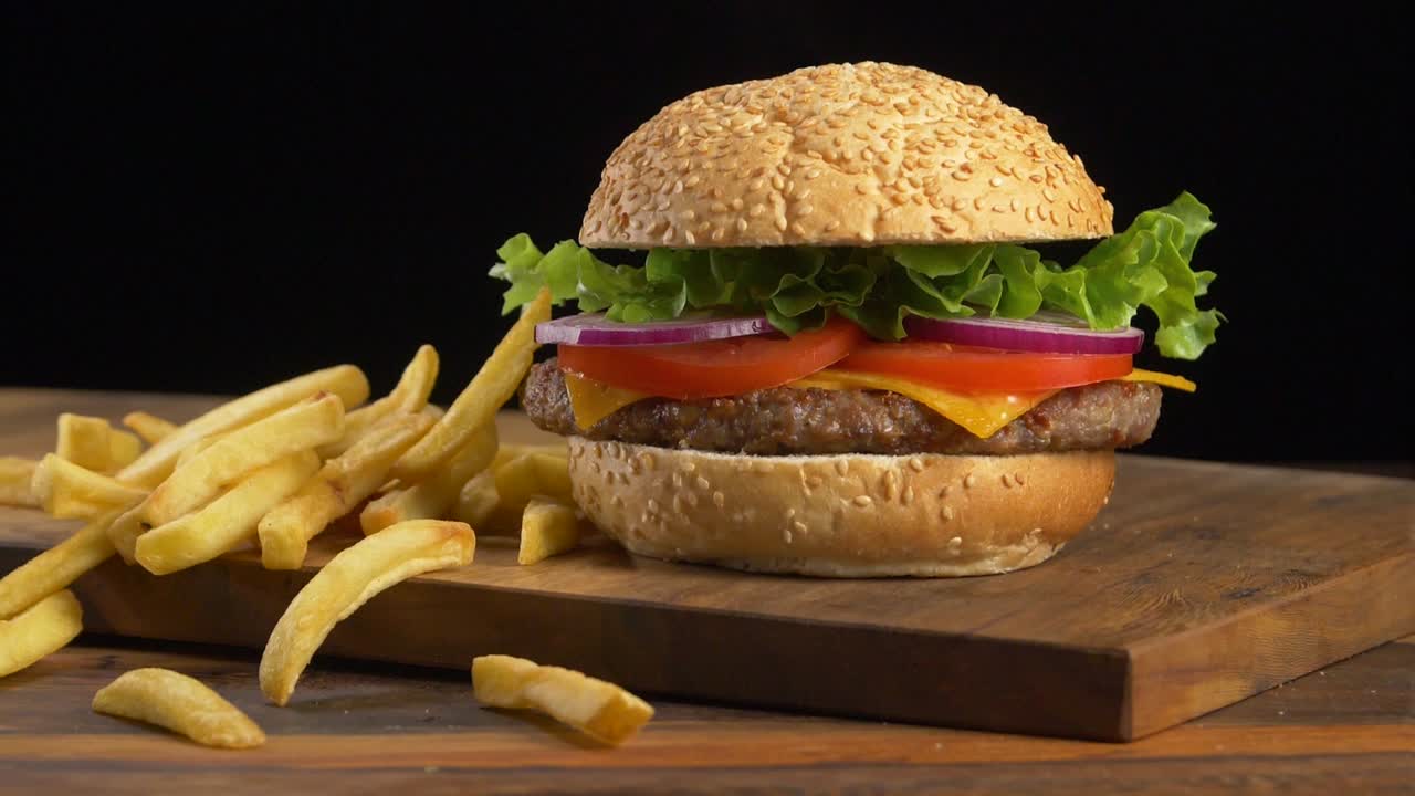 hamburguesa en una tabla de cortar con papas fritas cayendo a un lado