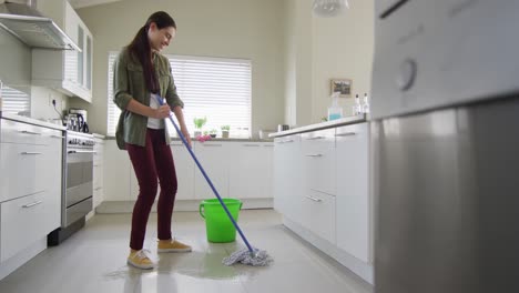 mujer caucásica feliz limpiando el piso con un trapeador y un cubo de agua en casa