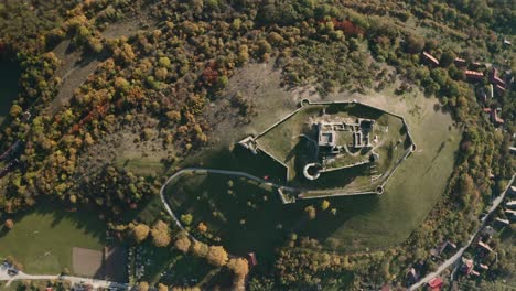 Birds-eye-vie-of-an-abandoned-ruined-Branc-castle-on-a-hill-above-a-village-with-an-autumn-forest,-Slovakia