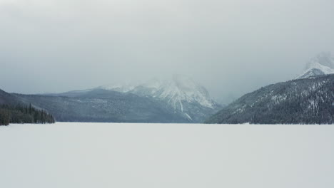 aerial moving low over frozen lake in winter with looming mountains behind