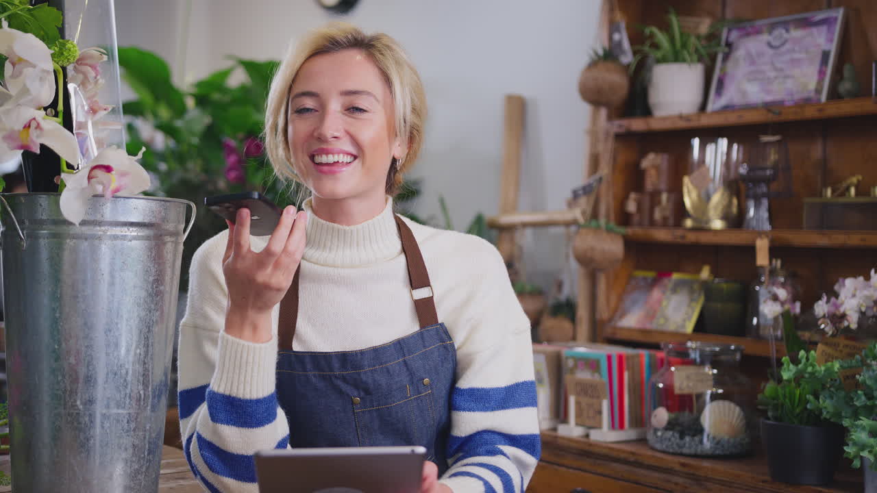Female Owner Of Florists Shop With Digital Tablet Talking On Mobile Phone