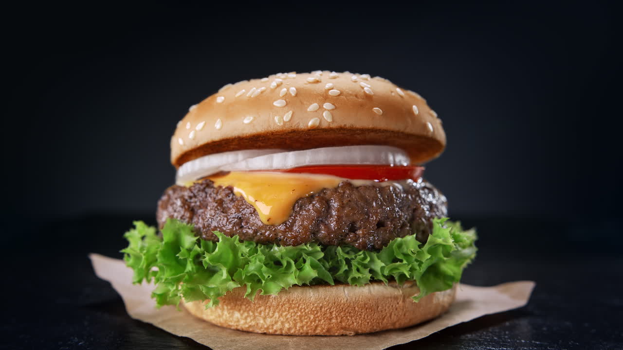 hamburguesa de carne en pan de sésamo tostado servida en una hoja de papel - fotografía en cámara lenta