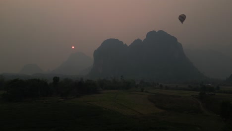 "aerial view at sunset over a mountain with a hot air balloon amidst the stunning backdrop of the sun's glow amid forest fire smoke