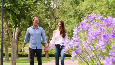 una pareja de adultos blancos caminando de la mano en un parque.