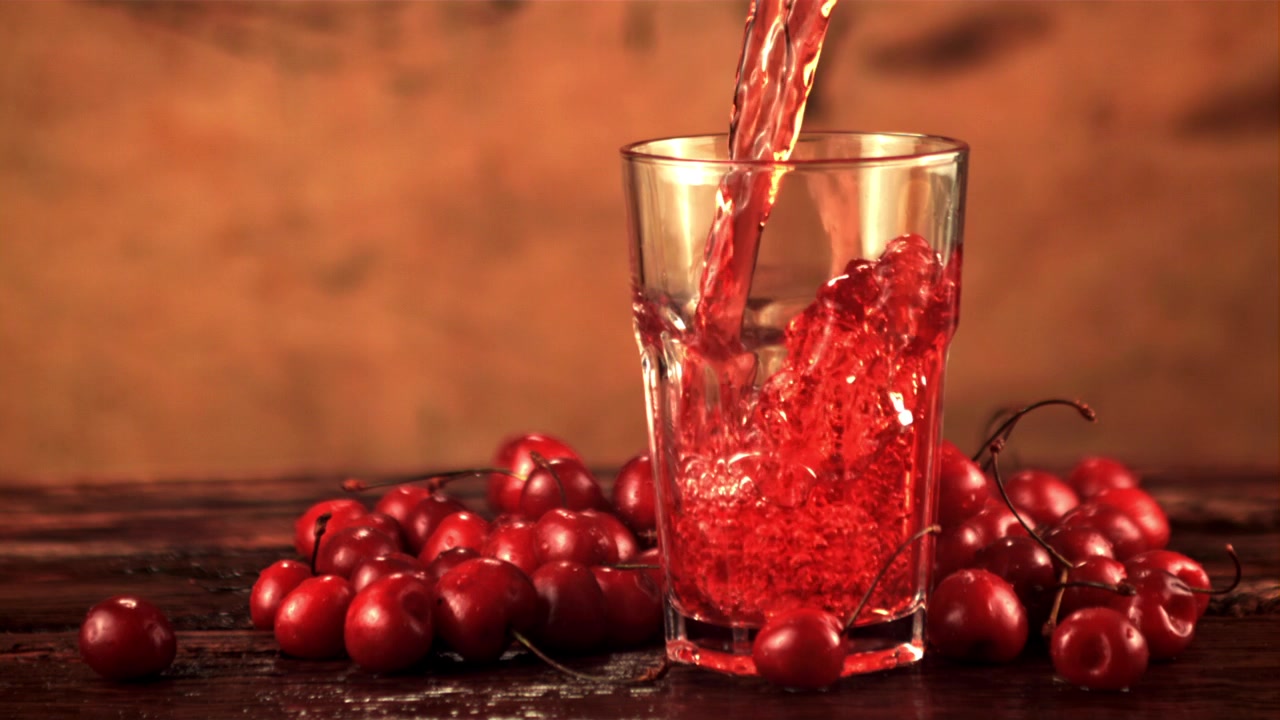 Succo di ciliegia rosso versato in un bicchiere con ciliegie fresche.