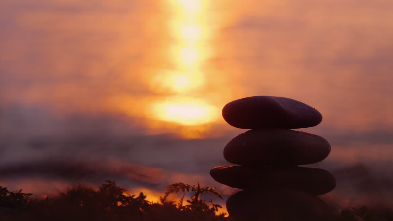 The Silhouette Of A Hand That Builds A Pyramid Of Stones Against The Background Of The Sea Where The