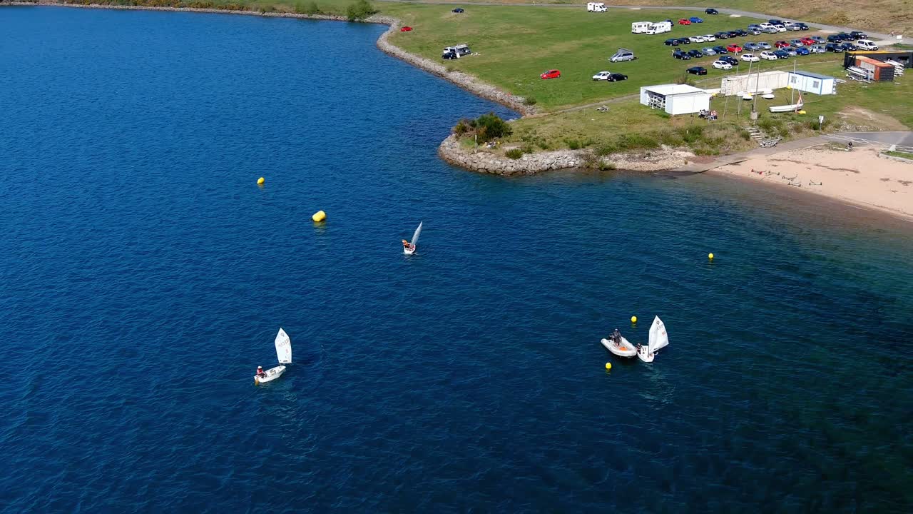 gente practicando en la escuela de vela del lago con playa, aparcamiento lleno de coches