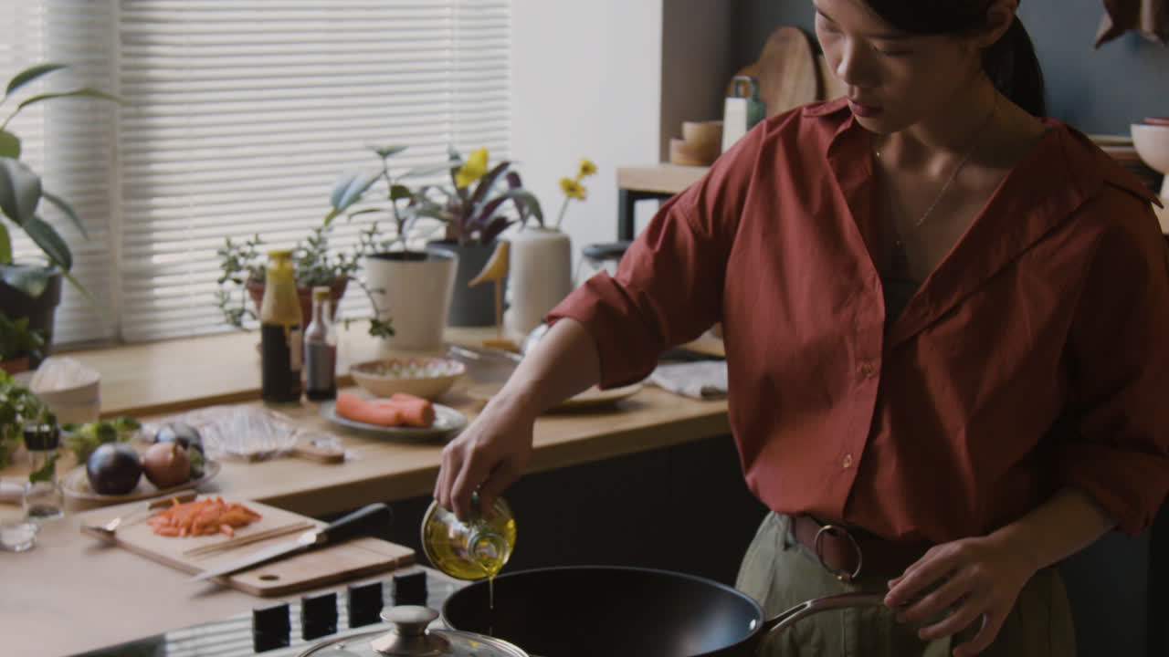 Woman cooking in a kitchen, pouring oil into a pan