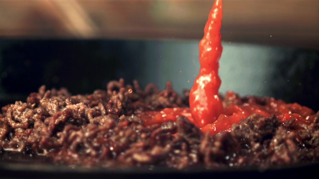 Versamento al rallentatore di salsa rossa su carne macinata cotta in padella.