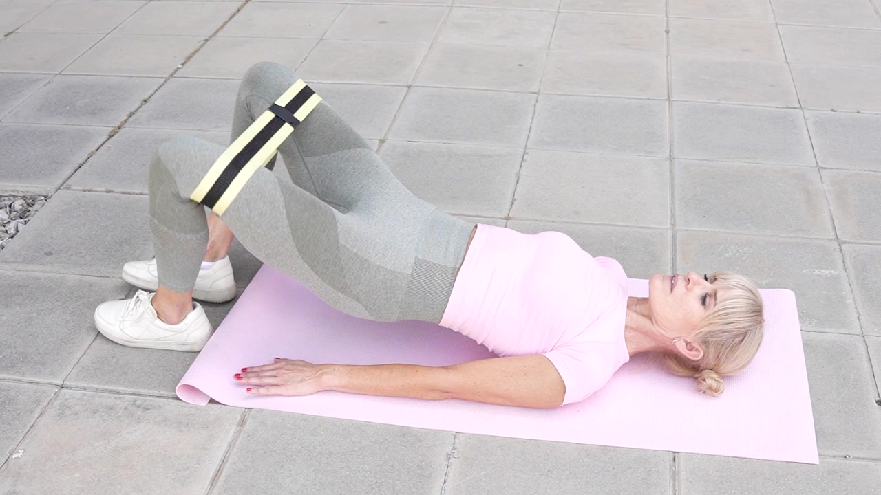 Una donna fitness esegue l'esercizio del ponte gluteo con un elastico fitness per la forza e la resistenza dei glutei.