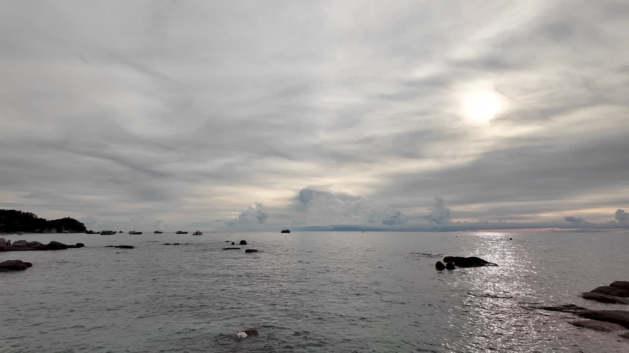 The sun shines through dramatic clouds over an ocean during the golden hour, creating a breathtaking scene with tranquil waters reflecting vibrant colors