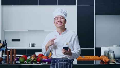chef sonriendo con un teléfono inteligente en la cocina