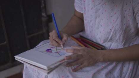 Girl-coloring-with-blue-colored-pencil-on-a-notepad