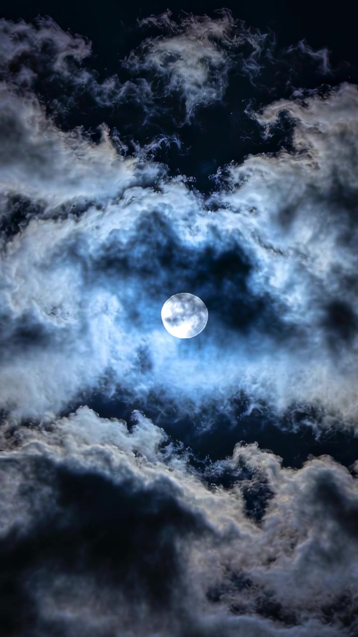 Video vertikal: Lapisan awan yang bergeser menyelimuti bulan purnama yang terang di langit malam, menciptakan lingkaran cahaya yang bercahaya