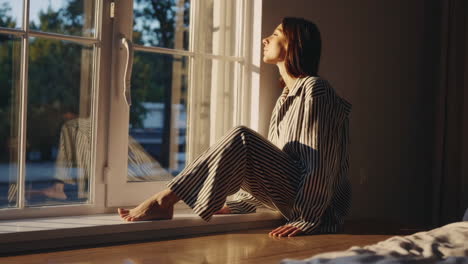 woman in pajamas sitting on window sill