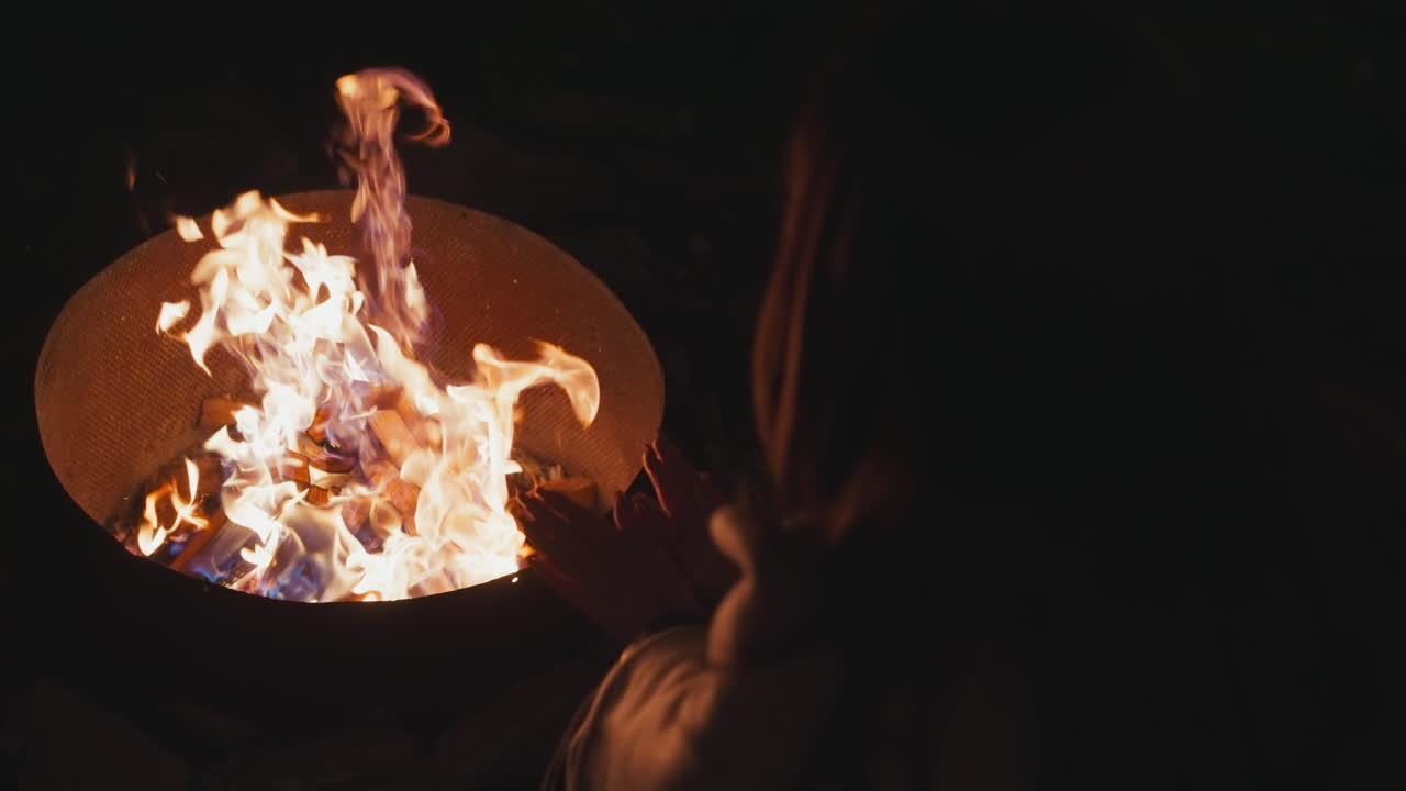 темный силуэт женщины согревает руки огнем в ночное время. прогулка и отдых в мире с природой во дворе загородного дома. сохранение тепла в холодную погоду