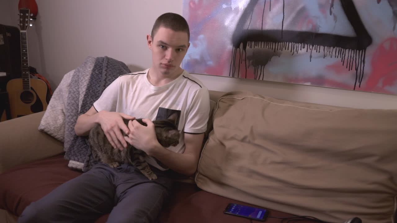 Young Man Sitting On An The Sofa And Playing With His Adorable Cat