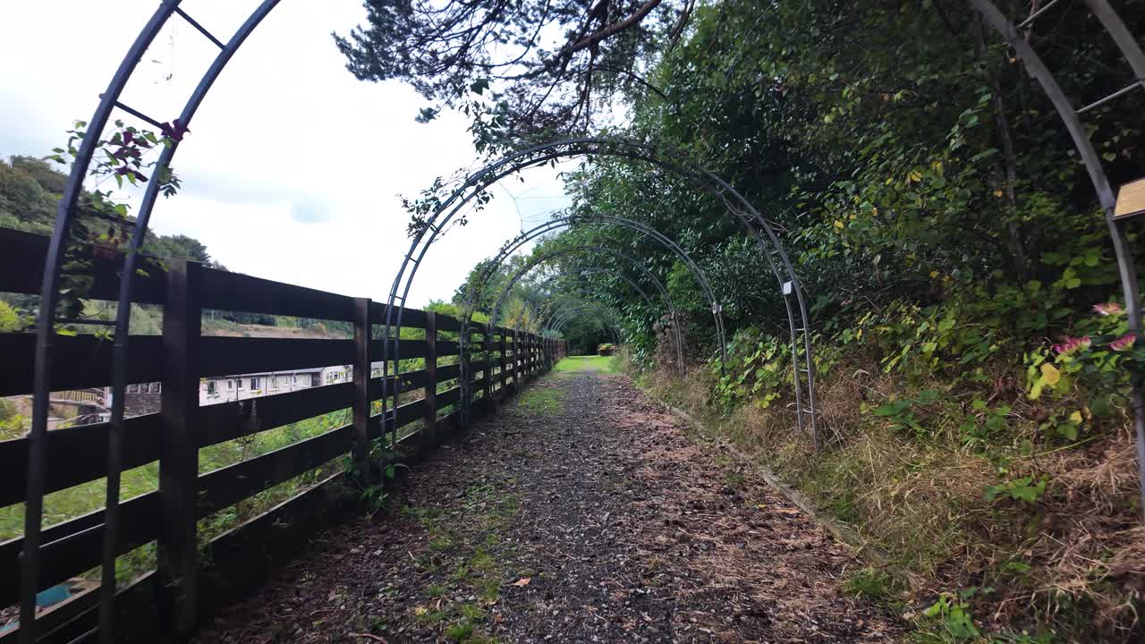 Rural trail leading through an archway tunnel next to a rustic fence