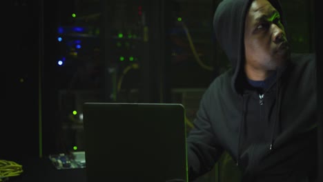 African-american-male-computer-hacker-using-laptop-in-business-server-room