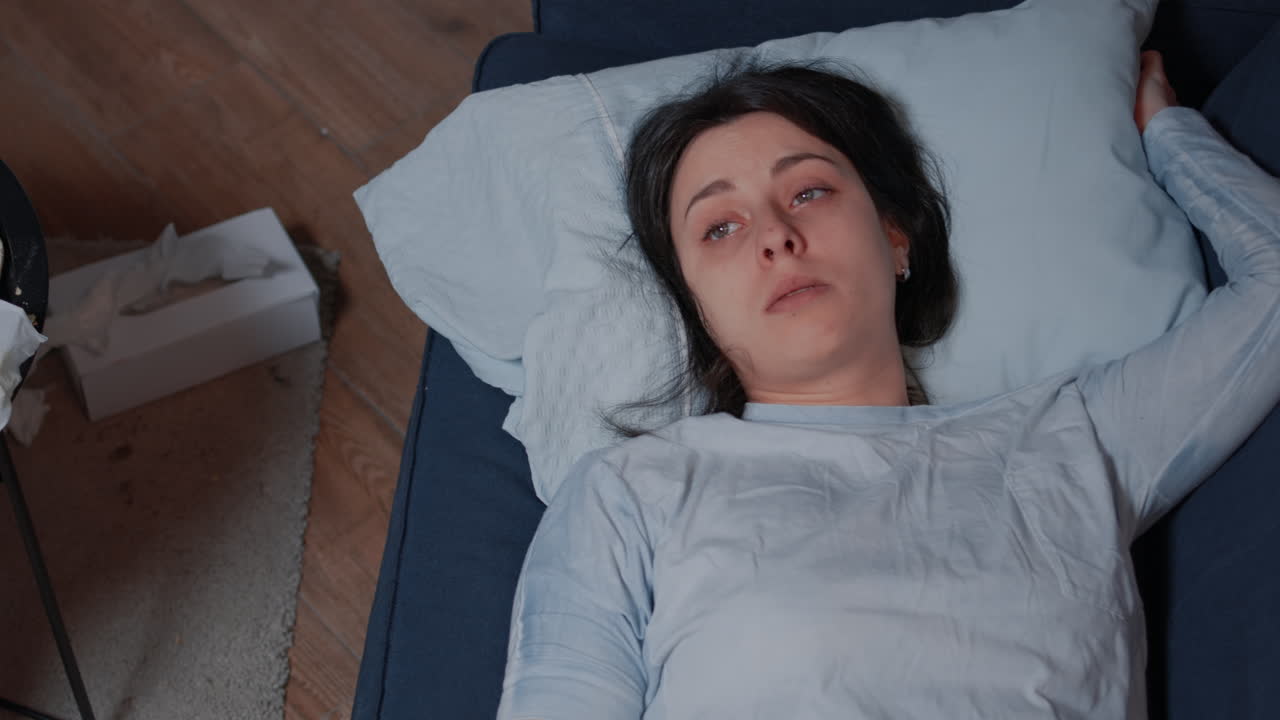 Depressed young woman sitting alone crying lying on sofa