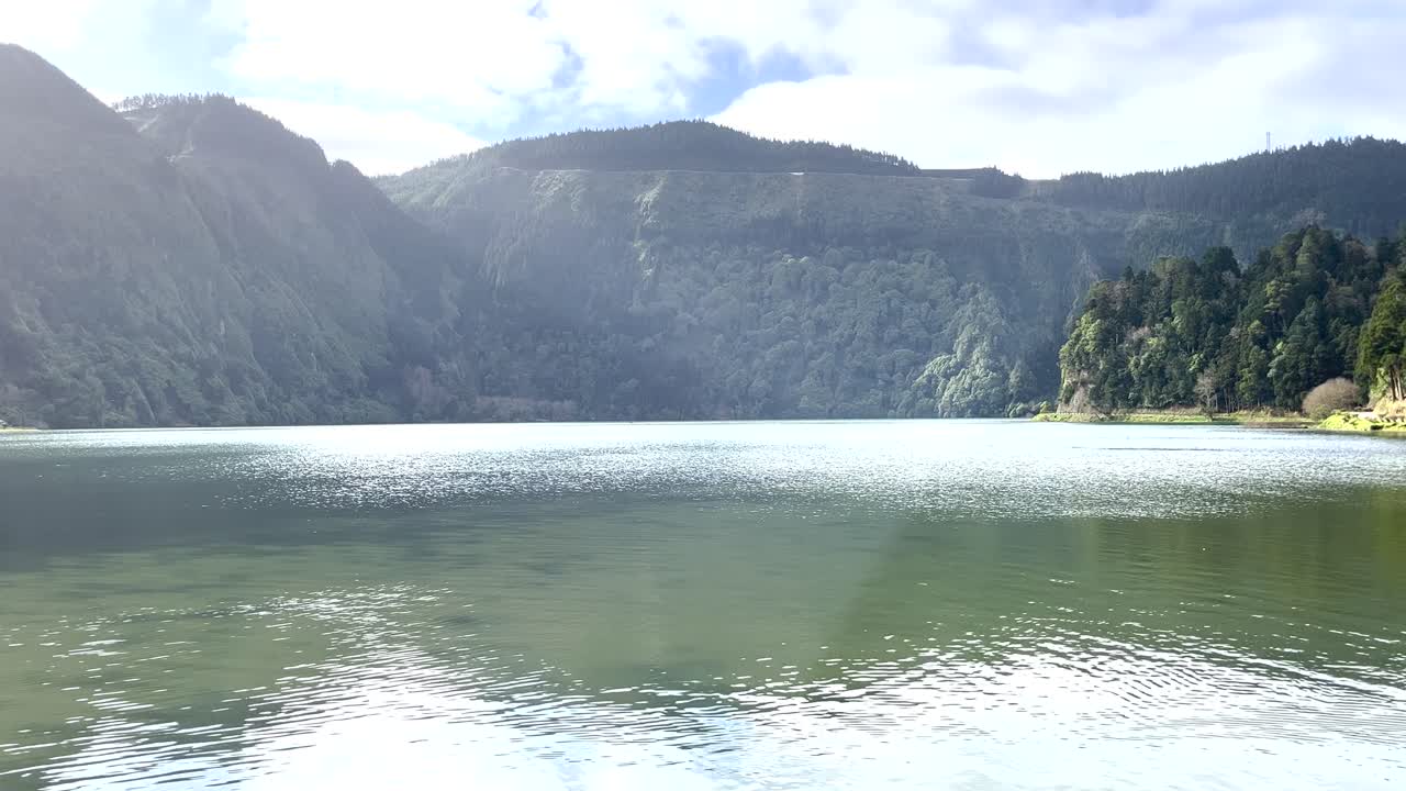 Aerial video over a very calm river with light reflections on the water, surrounded by trees in the Azores, Portugal