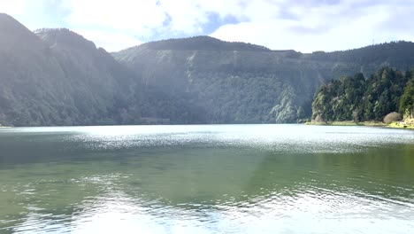 aerial video over a very calm river with light reflections on the water, surrounded by trees in the azores, portugal