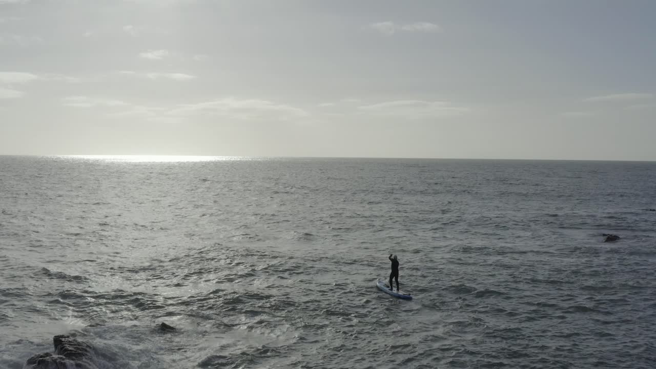 바위 섬 근처 고르지 못한 회색 바다에 패들 보드 남성, 공중