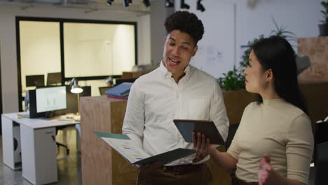 biracial man and asian woman discuss business work in an office