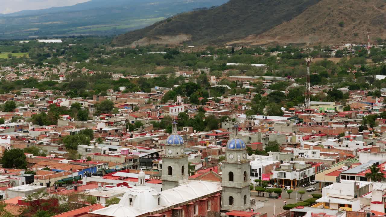 Backward flight overlooking the bell towers of the San Juan de Bautista church in Tuxpan Jalisco. Ascending view reveals panoramic perspective of the city